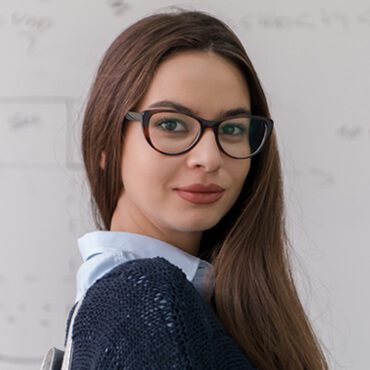 A woman with glasses and long hair wearing a blue shirt.