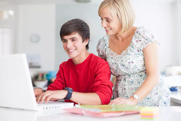 A woman and boy using laptop computer at table.