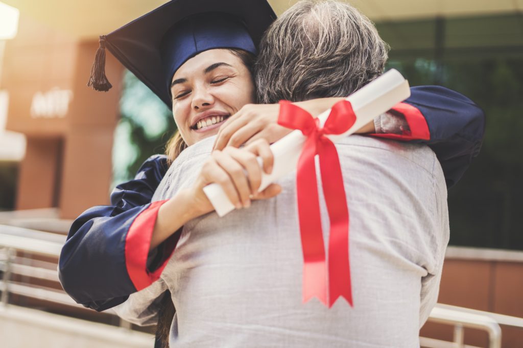 A woman hugging an older man with a diploma.